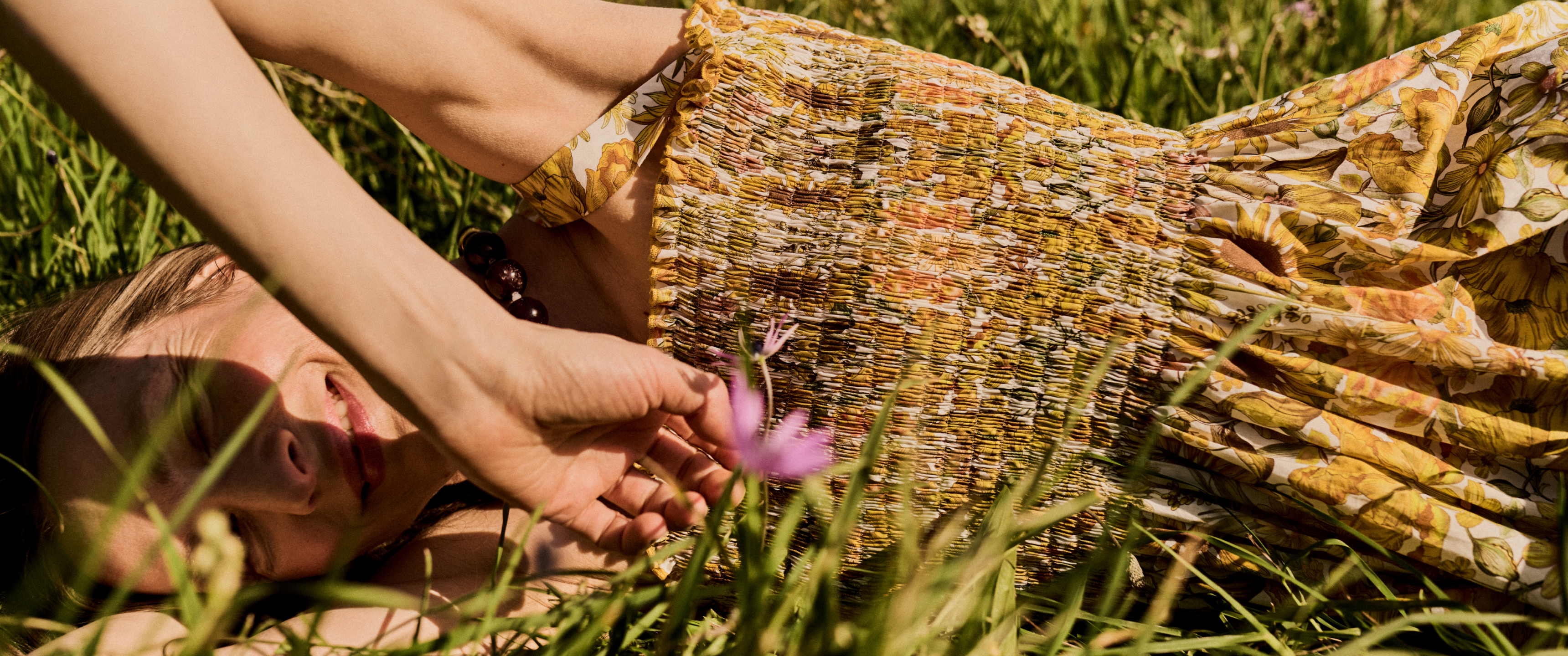 Model lying in the grass wearing a summer ruched dress from Liberty