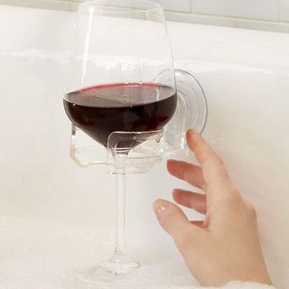 A person's hand reaching for a wine glass that's placed in a clear plastic suction cup holder on the bath wall 