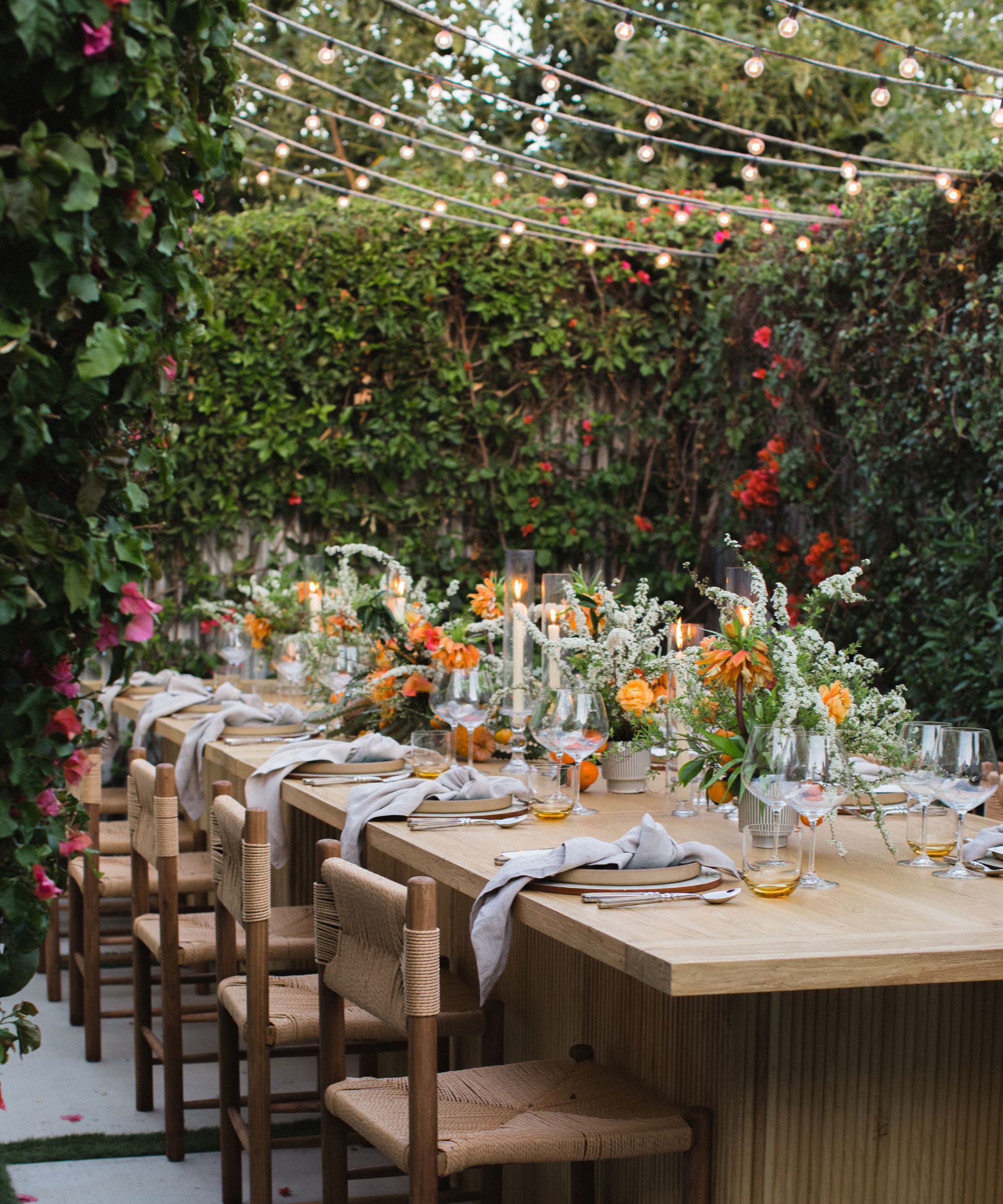 Outdoor table layout with orange flowers and string lights overhead