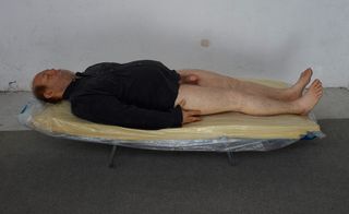 A man is lying on a lounge bed. He appears to be sleeping. He has a black long sleeve shirt on, while the bottom part of the body is completely naked.