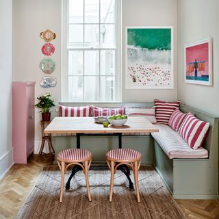 small corner of open plan kitchen with pink white and green artwork which defines the scheme of the green banquette pink and white striped cushions