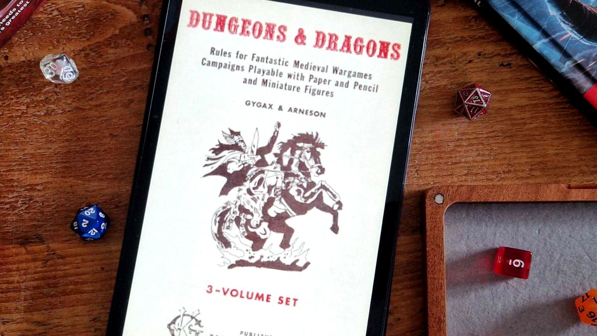 An original Dungeons &amp; Dragons Player&#039;s Handbook on a tablet sat on a wooden table, surrounded by dice, a dice tray, and other books