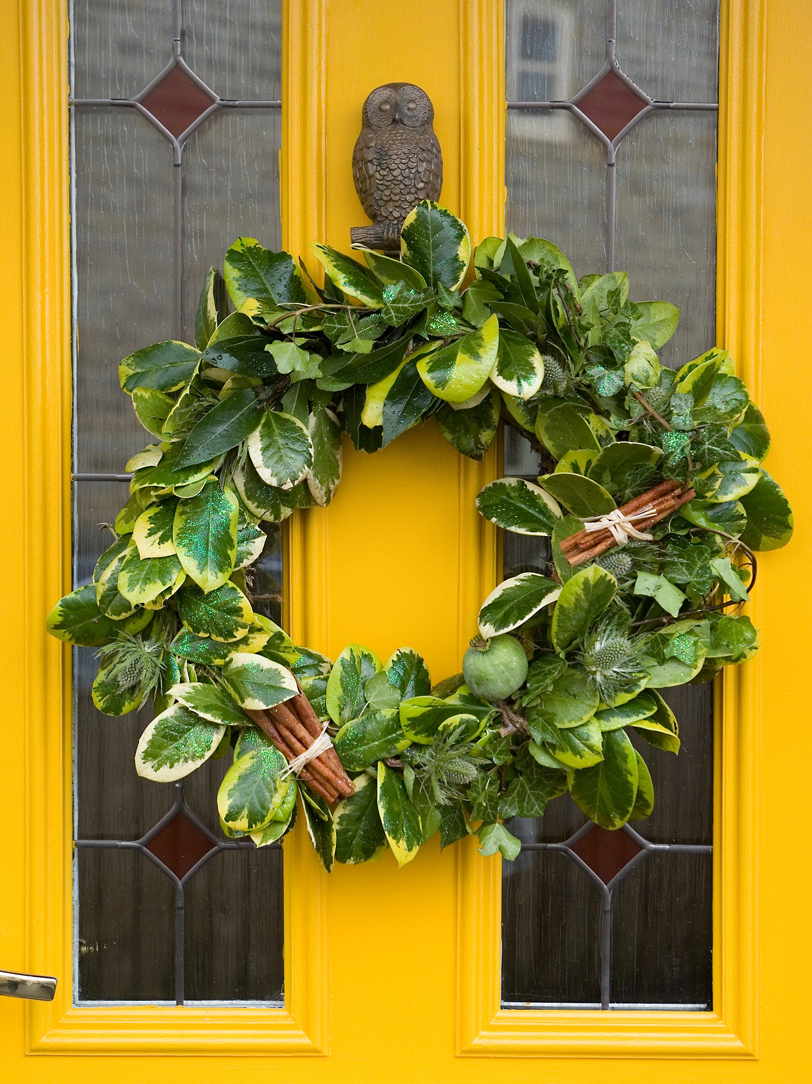 Closeup of winter wreath hanging on bright yellow front door, with frosted glass panes and owl door knocker.