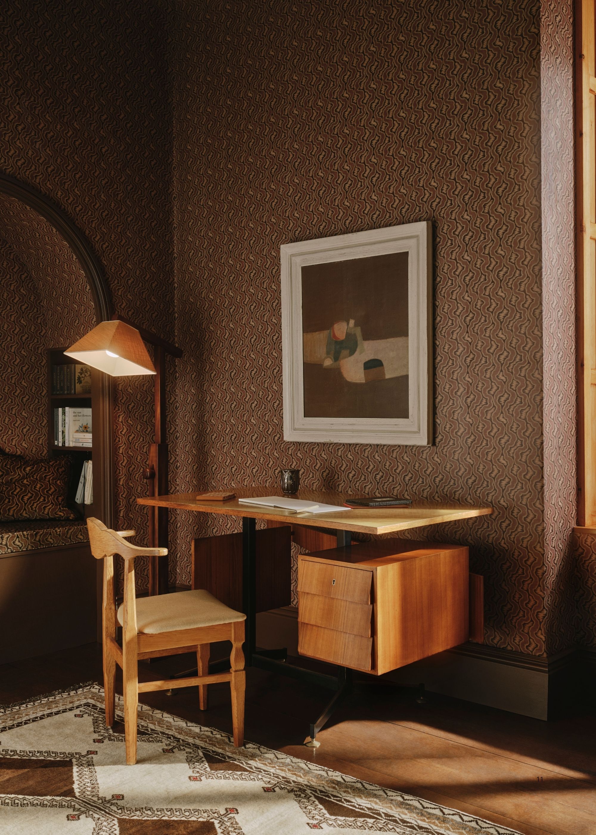 A home office room with brown patterned wallpaper, wooden flooring, a white and brown rug, and a wooden floating desk and matching chair.