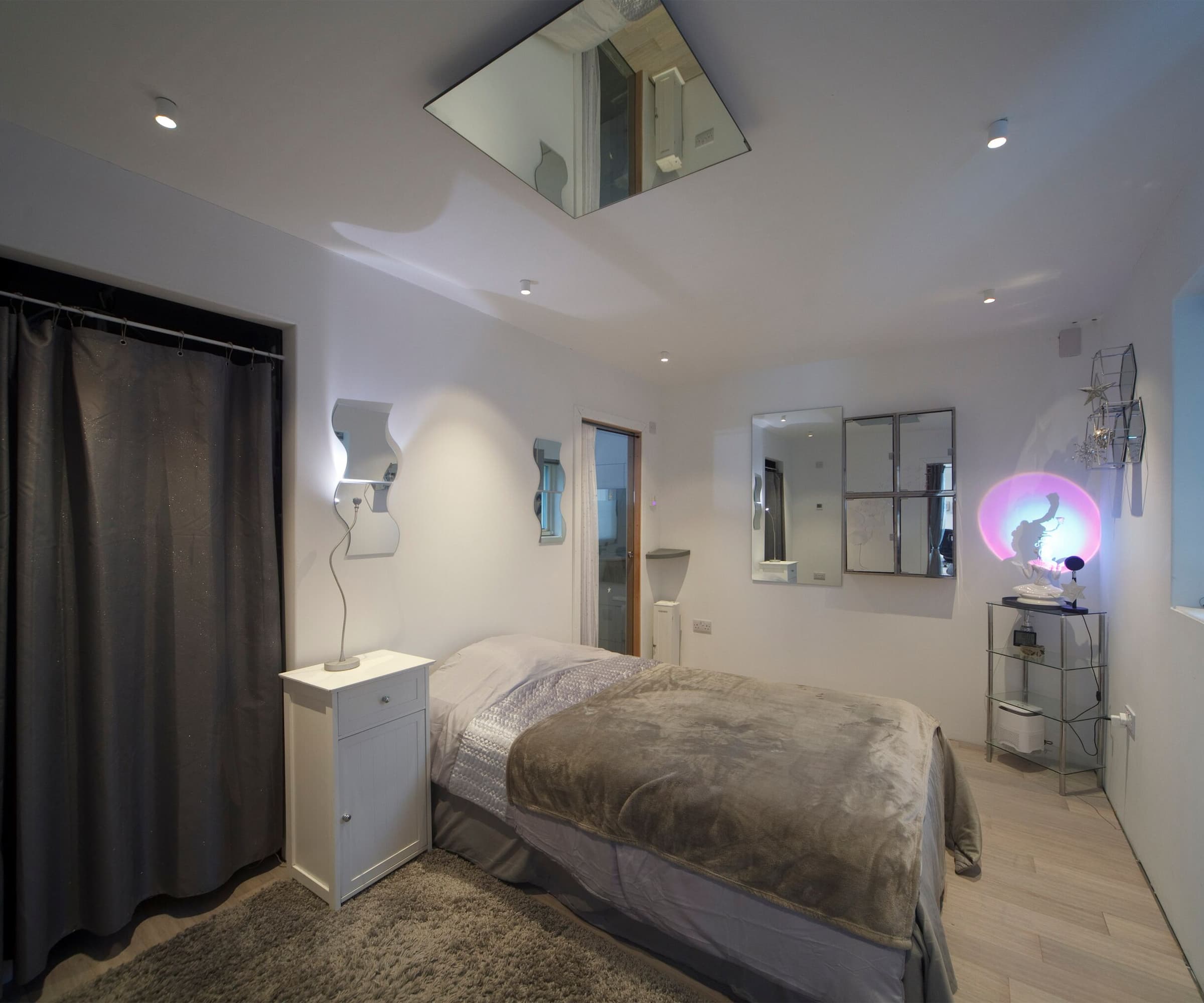 A bedroom with a mirror on the ceiling and grey curtains with an en suite bathroom