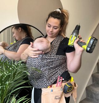 Mother with her baby with screwdriver in her hand standing next to plant in front of the stairs