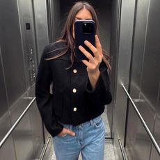 Influencer Maja Weyhe poses for an elevator selfie wearing a round neck cropped black jacket with gold buttons paired with jeans