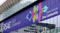 A telephoto shot of the RSAC Conference 2025 banner on the side of the Moscone Center in San Francisco. Next to a stylized waveform, the words "Many Voices. One Community." are written in white.