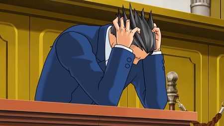 Phoenix Wright holds his head in his hands in the courtroom, clearly in distress.