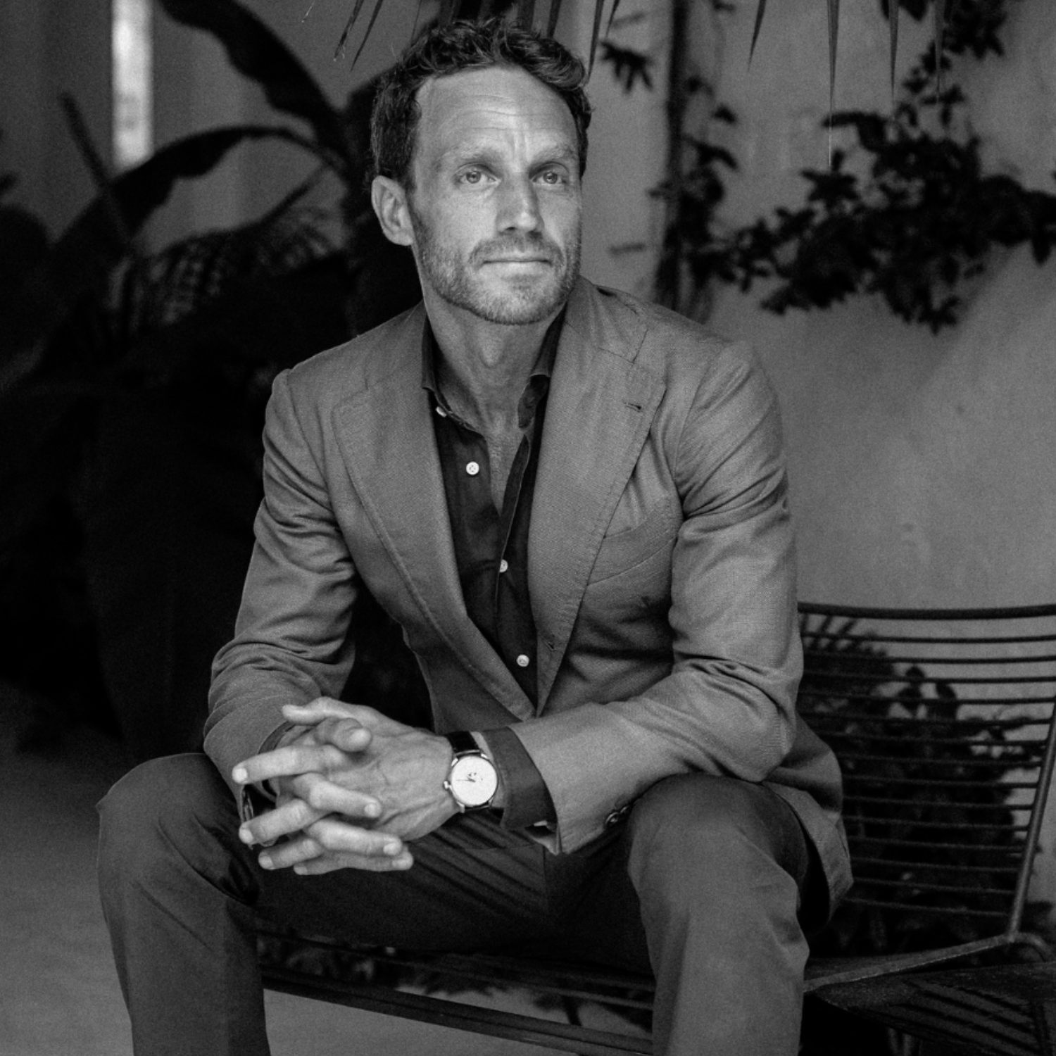A black and white photo of a man in a suit sitting on a metal chair