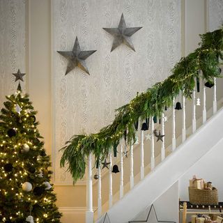 White staircase topped with green en plant Christmas décor and a Christmas tree with fairy lights