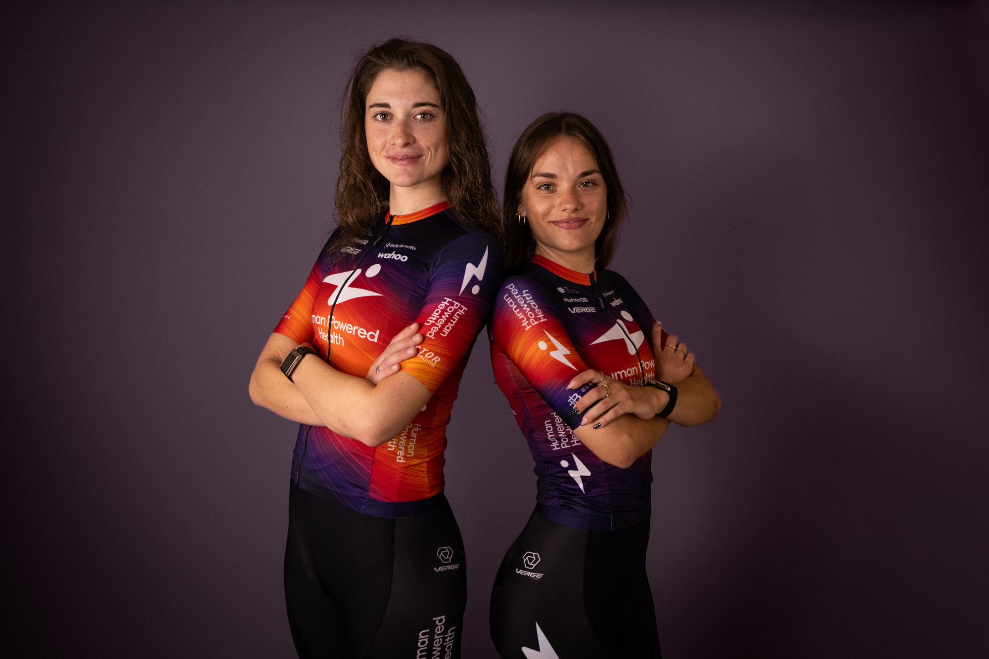 Human Powered Health riders pose in new 2026 team kit, a blend of purple and orange