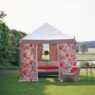 Floral printed marquee with neutral sofa, chair and red cushions