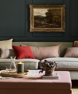 A dark green room with a gray sofa and pink ottoman with a cozy vignette