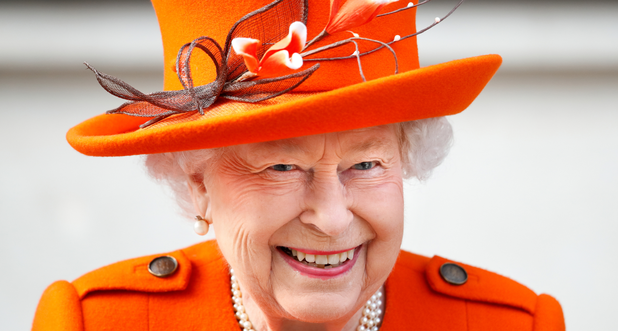 Queen Elizabeth smiling in an orange coat and hat