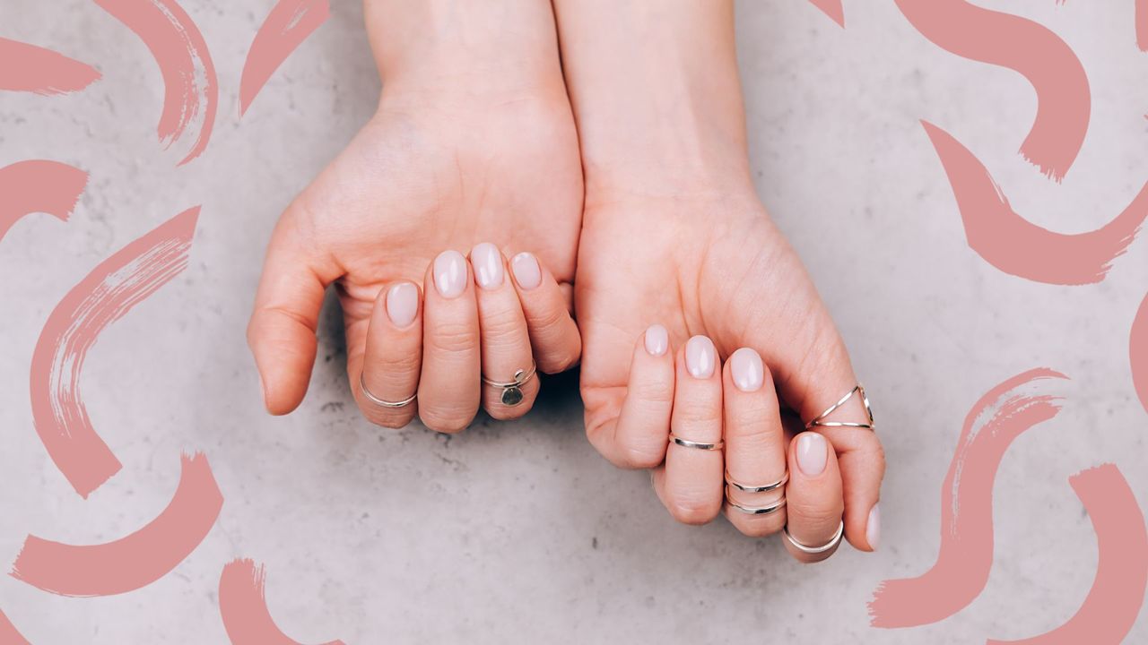 A woman&#039;s hand with natural dip powder nails and lots of rings on a marble backdrop