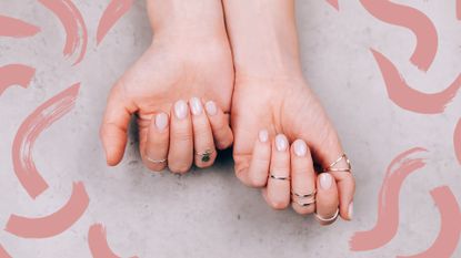 A woman's hand with natural dip powder nails and lots of rings on a marble backdrop