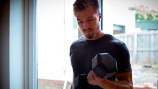 Man performs biceps curl with a dumbbell at home