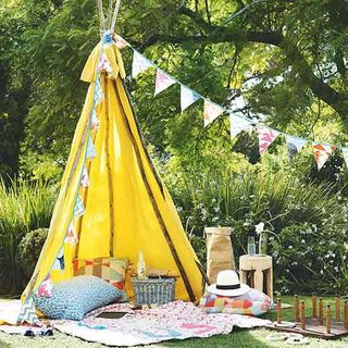 yellow teepee tent with bunting cushion and green plant