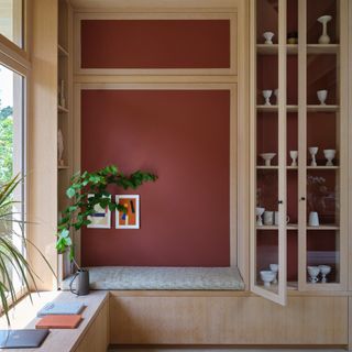 A built-in display cabinet and bench with the wall behind painted in Etruscan Red by Farrow & Ball