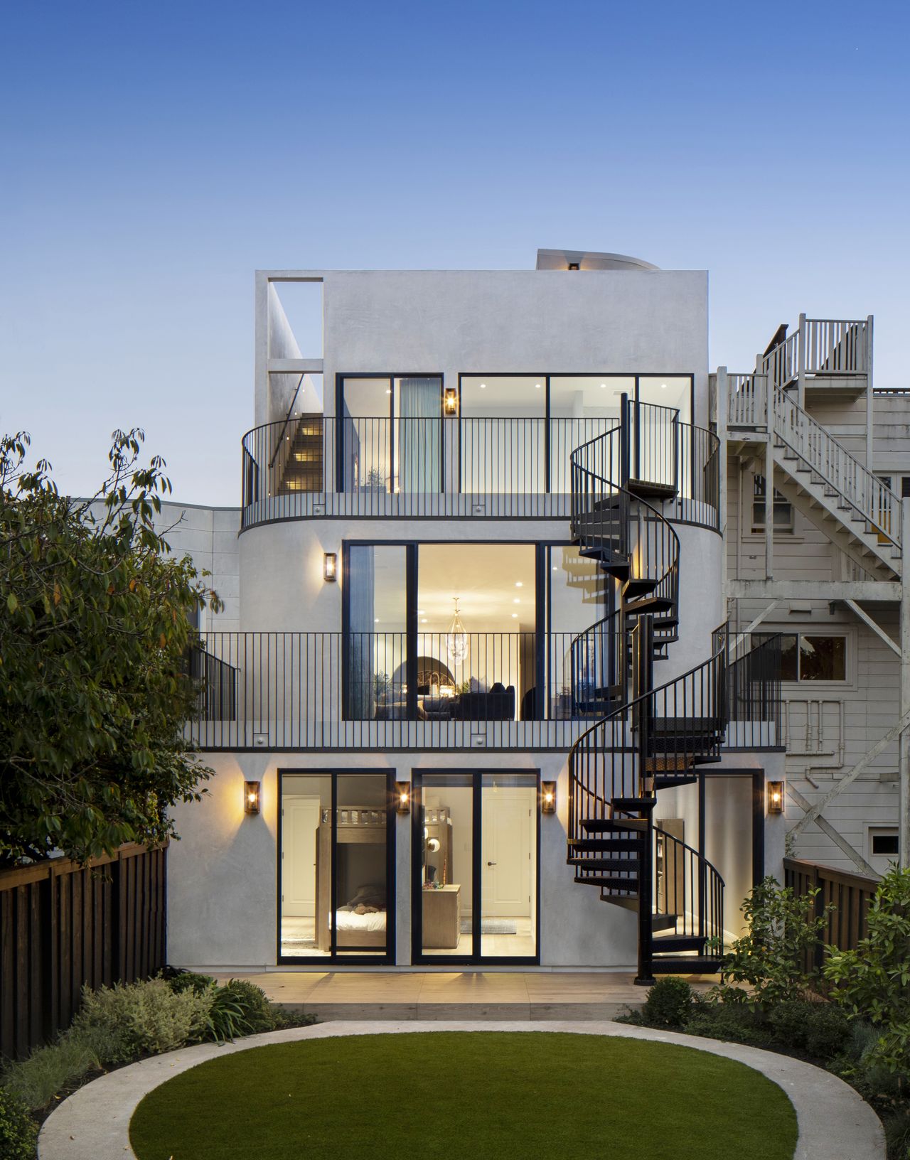 Exterior shot rom backyard of modern house with large glass windows at dusk