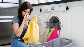 A woman holding her nose while pulling laundry from a washing machine