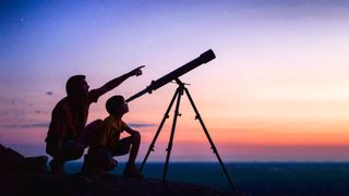A young boy looking through a telescope at sunset with his father.