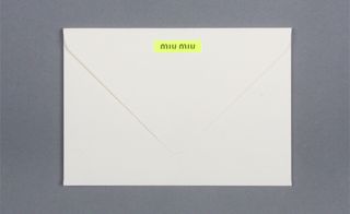 View of ﻿Miu Miu's white and yellow invitation envelope pictured against a grey background