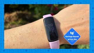 The image shows a woman's wrist with a pale pink Fitbit Inspire 3on it. Inset, a Tom's Guide Savings Squad Prime Day deal badge is shown in blue