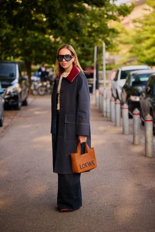 Gaya jalanan Copenhagen Fashion Week. Seorang wanita mengenakan jaket denim dengan kerah merah, celana jins biru, dan tas loewe dari rafia.