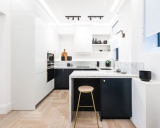 A u-shaped kitchen with a peninsula with black and white cabinets and a simple bar stool