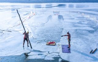 Two men move chunks of ice to create an area for swimming at a lake in Shenyang, China