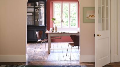 Entryway with open door leading through archway to dining area. It has wooden flooring throughout, a blue woven runner in hallway and a terracotta colored feature wall in the background