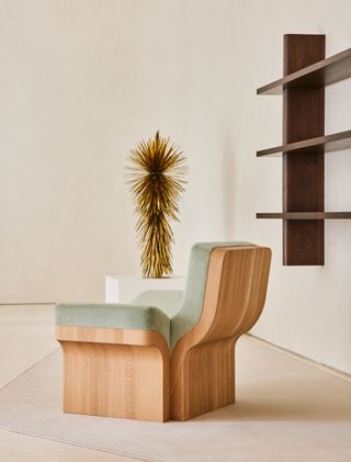 A wooden chair in the foreground with dark wooden shelves on the wall and golden leaves sculpture in the background