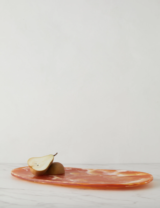 orange cheese board laying on a flat surface with a halved pear on top