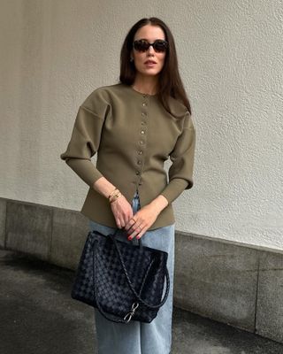 Woman wears waisted cardigan, blue jeans and black bag