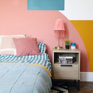 Bedroom with pink, orange, and blue accent feature wall, bed and bedside table with pink table lamp