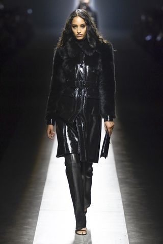 A model on the Tom Ford runway wearing a dark trench coat