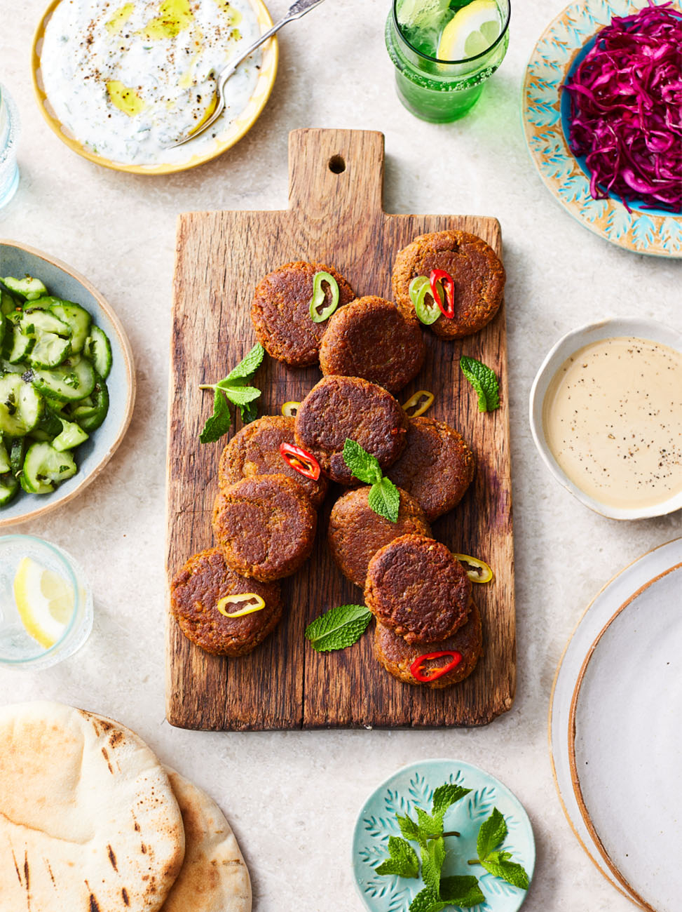A wooden board laden with falafel and surrounded by plates of flatbread
