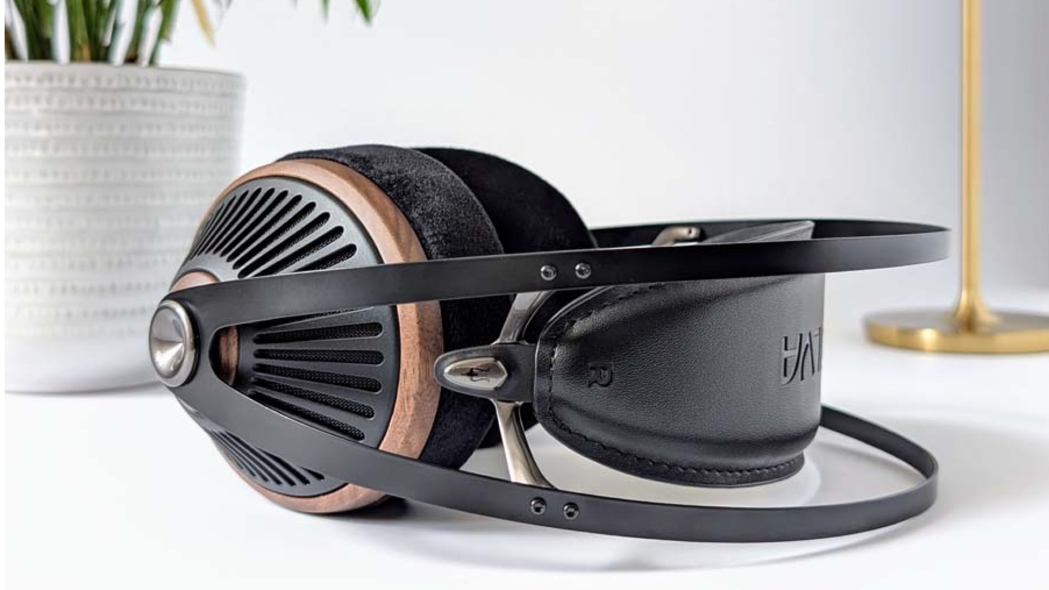 A pair of Meze Audio 105 Silva headphones on top of a white desk or unit with a plant pot and a lamp in the background