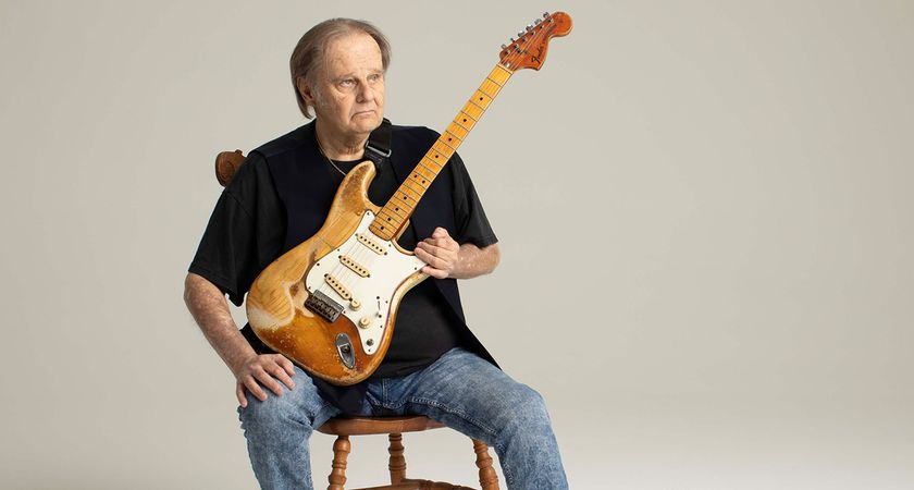 Blues veteran Walter Trout photographed seated with a beat-up old Strat.