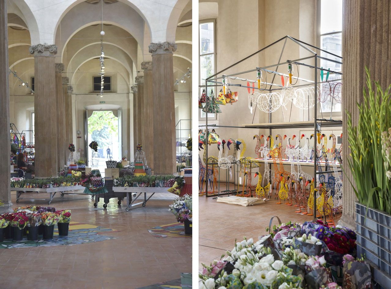 Flower market with buckets of flowers some on the tiled floor and some on trailers with wheels on the left and geese and other birds decorations with more flowers on the right