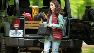A woman in camping clothes lifts a DELTA mini portable power station out of the back of a Jeep.