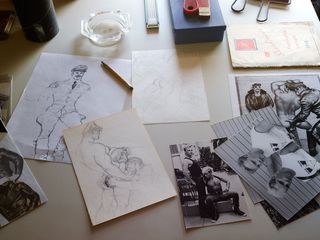White table top, black and white male photographs, yellow pencil, glass ashtray, male erotic sketches, small blue box