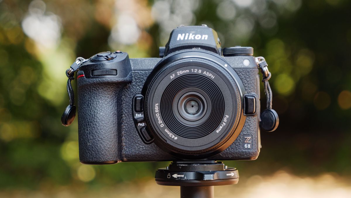 Viltrox AF 26mm F2.8 EVO 'pancake' lens attached to a Nikon mirrorless camera, there's dappled light through a tree behind it. No lens cap or filter