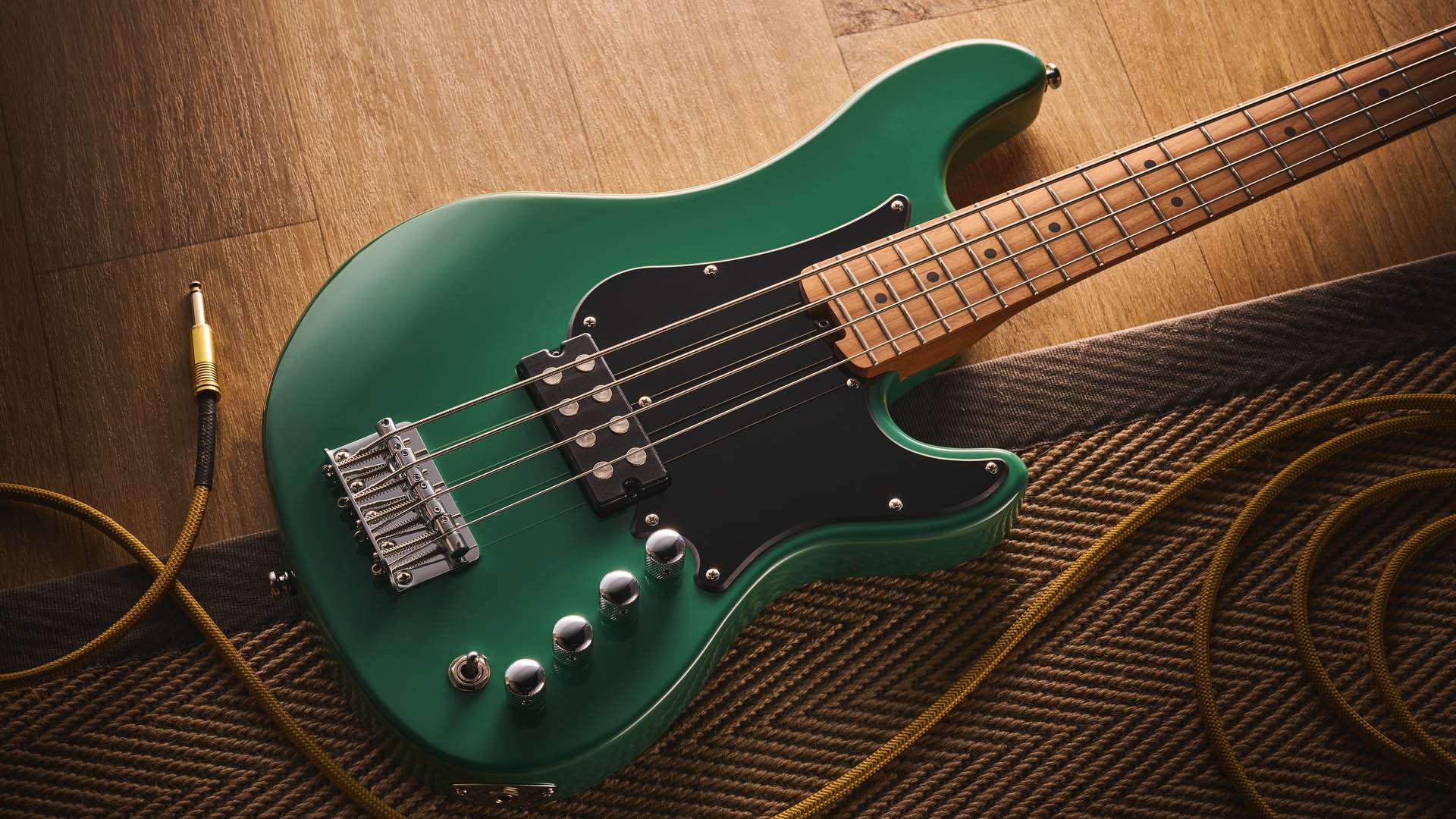 The Cort GB Short-scale Bass finished in green, photographed against a light wooden floor and rug.