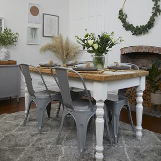 White dining room with a white-legged kitchen table with a wooden top and grey chairs, with floral décor next to a fire place