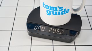 a luxury coffee scale made by Felicita Arc is photographed against a blue background with its weight, USB-C cable, and silicone mat