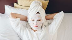 A woman with a face mask on and a towel on her head resting while on vacation. 