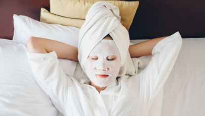A woman with a face mask on and a towel on her head resting while on vacation.